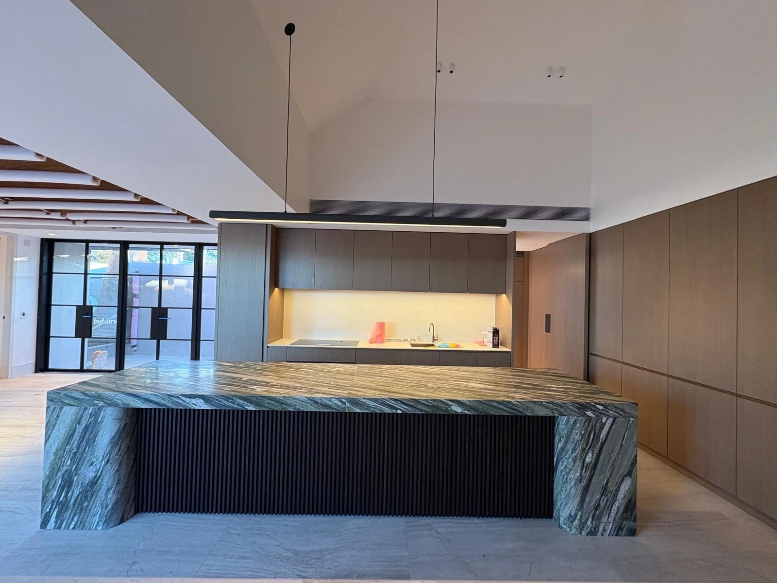 Modern kitchen with large marble island bench and warm wood cabinetry.